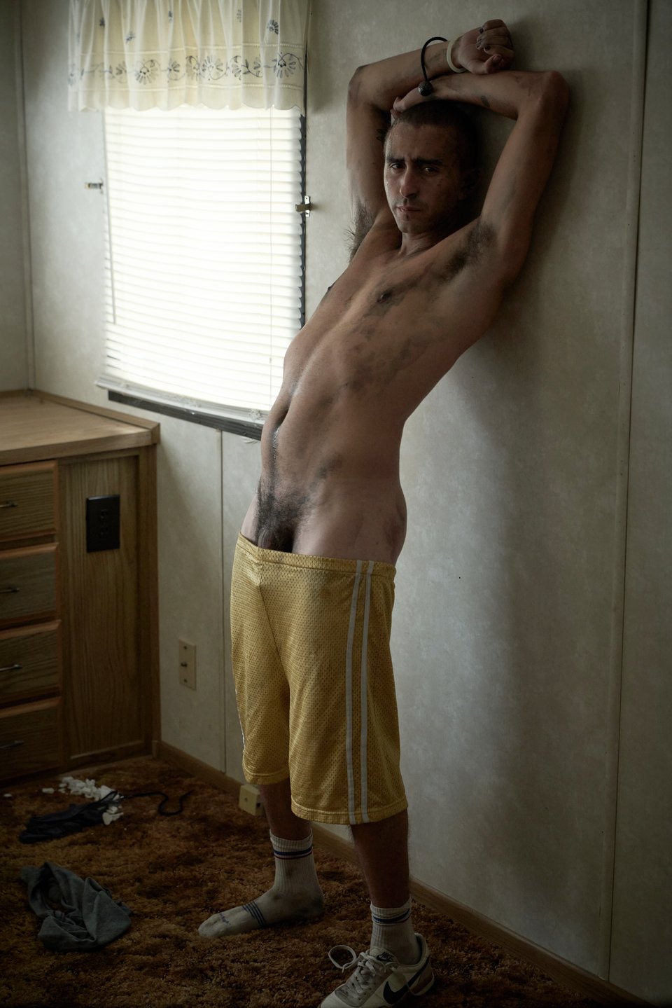 shaved head beck stands with arms raised and gold gym shorts pulled down low