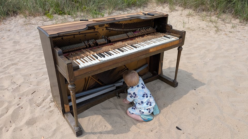 A small child in a Mickey Mouse two-piece playing with a decrepit piano on a beach.