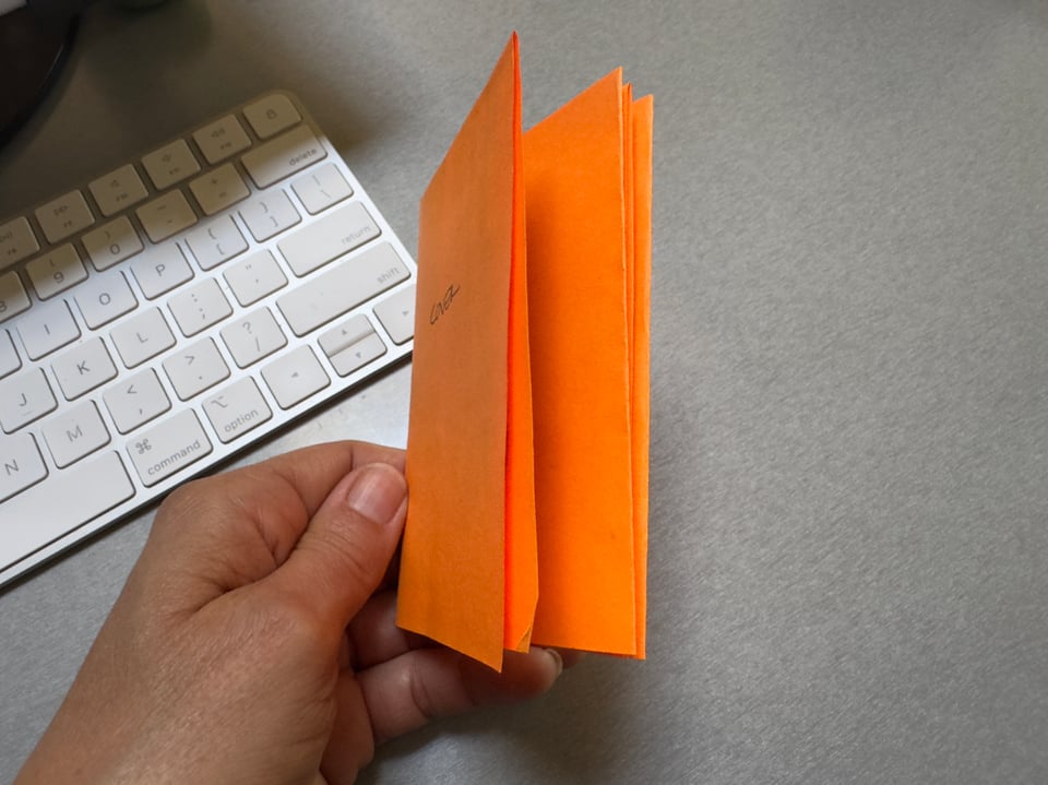 Hand holding orange paper booklet with keyboard in the background