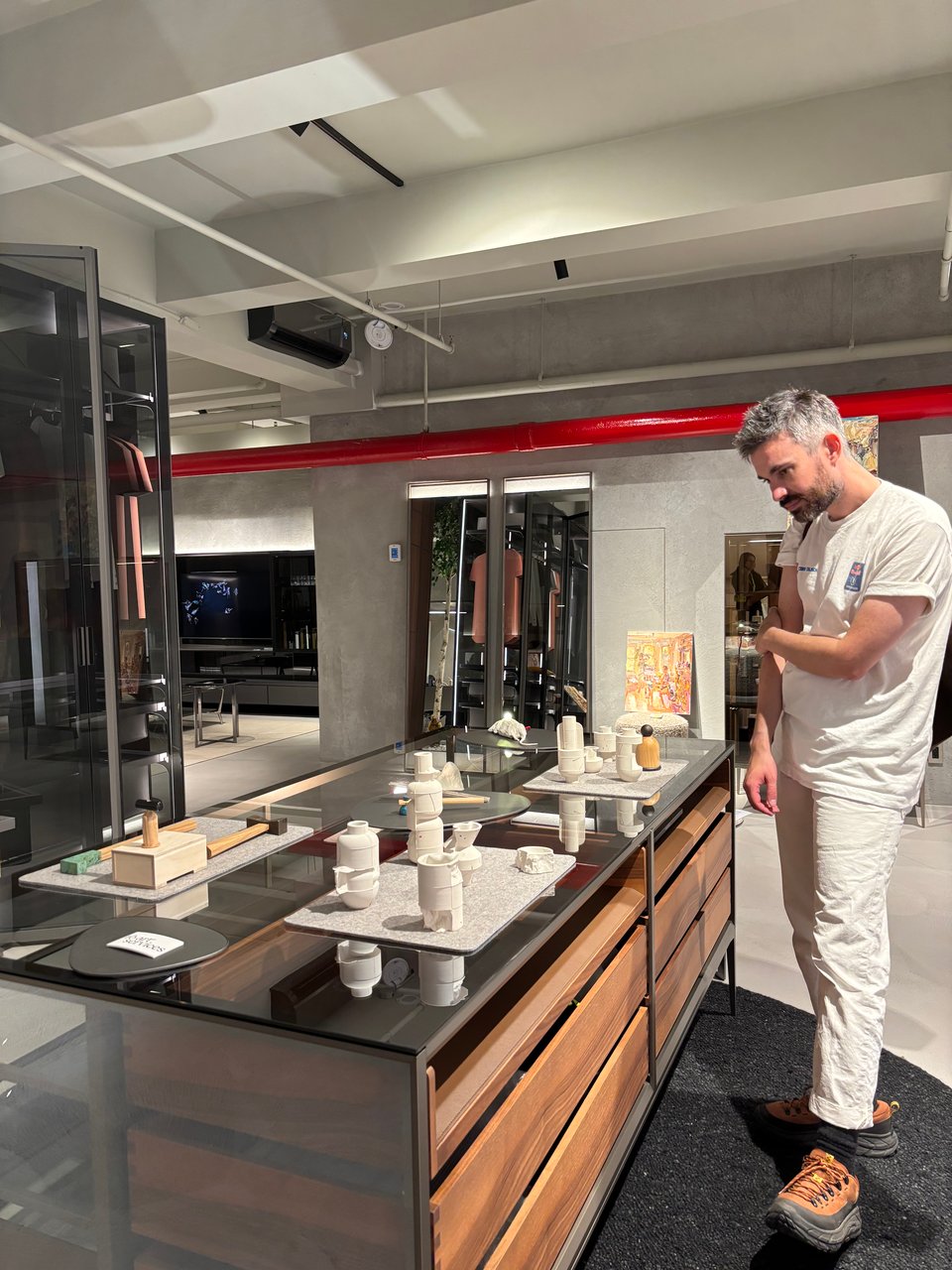 Todd stands in front of a table covered in various small sculptures. He is wearing all white, and the bulk of the sculptures are all white.