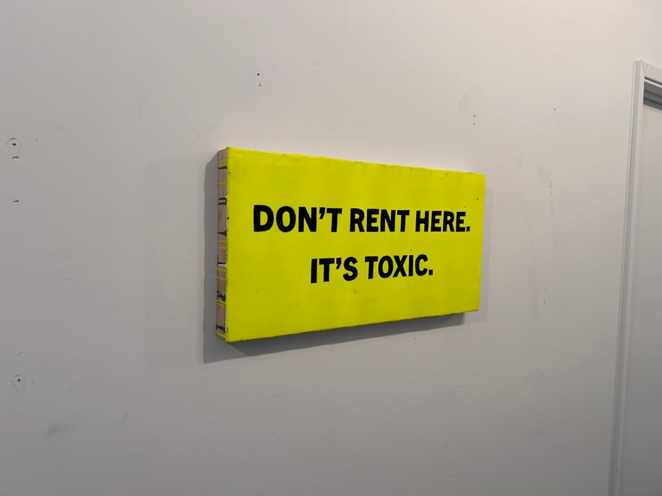 Horizontal painting. Yellow background. Black text that says DON'T RENT HERE. IT'S TOXIC.