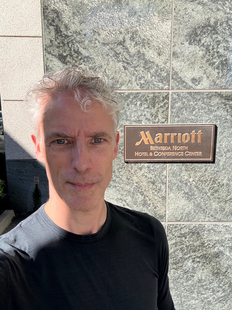 selfie of white man in black long-sleeved T-shirt beside a wall with a plaque reading, "MARRIOTT BETHESDA NORTH HOTEL & CONFERENCE CENTER"