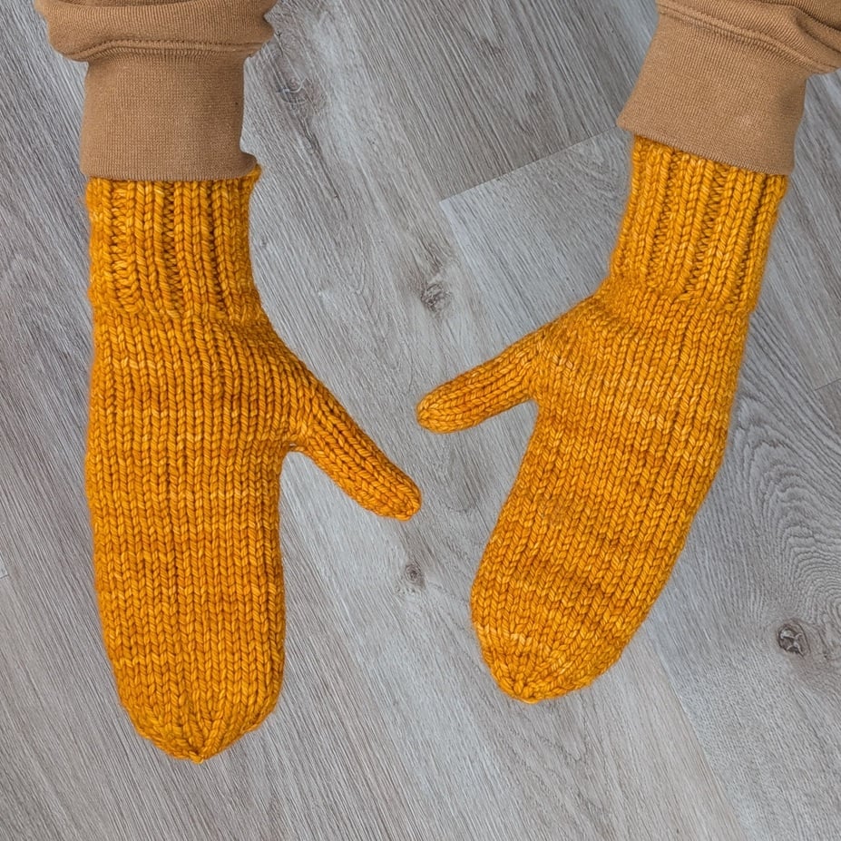 Two long hands model a pair of golden yellow hand-knit mittens. Iris's hands are SO long.