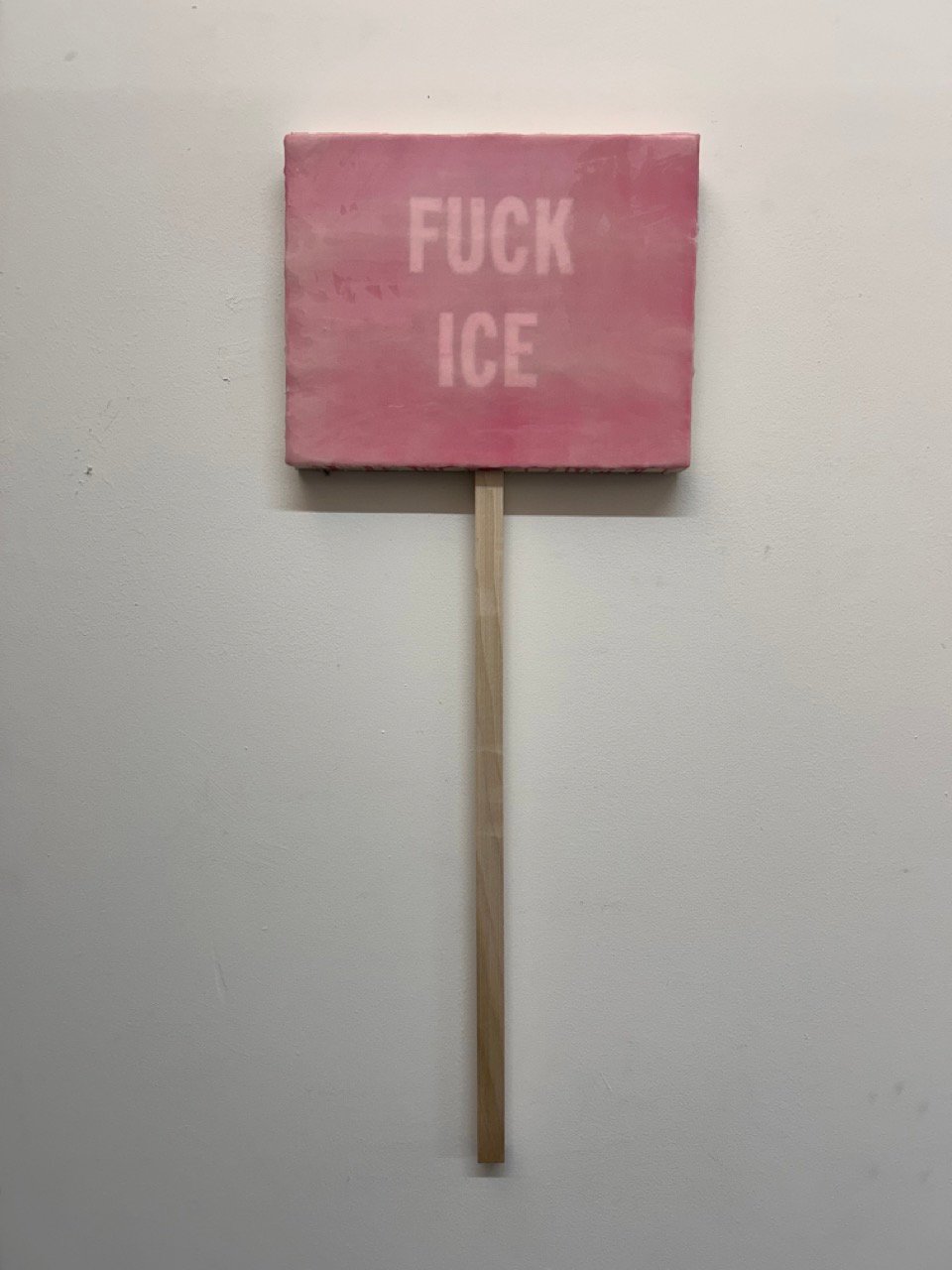 A painting with a stick attached, so it looks like a protest sign. The background is pink, and in lighter pink it says FUCK ICE.