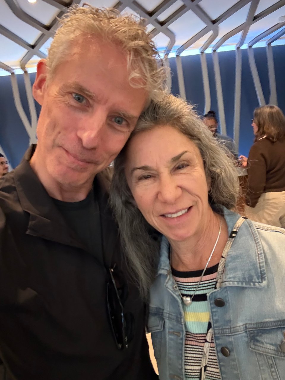 double-selfie of white man and woman, smiling; she's in a faded denim jacket with a striped sweater, and he's in a long-sleeved black T-shirt with a thin black running jacket over it