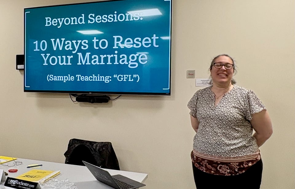Regina Howland smiles while standing next to her presentation slide, Beyond Sessions: 10 Ways to Reset Your Marriage”.