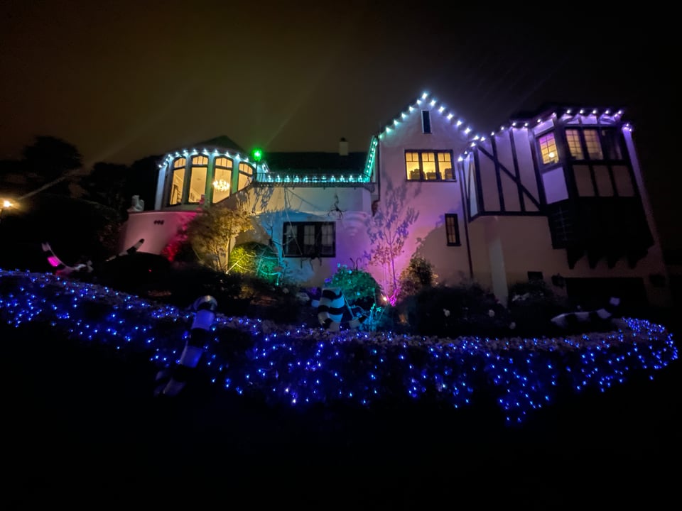 A house is lit up with multi colored string lights for Halloween. Mostly Purple and Turquoise.