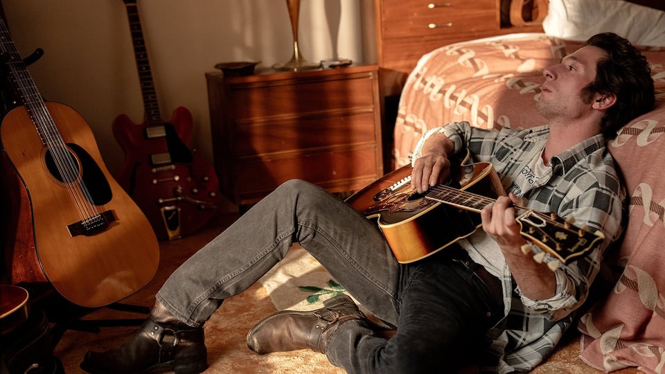A scene from Springsteen: Deliver Me from Nowhere where Bruce is on the floor playing a guitar.