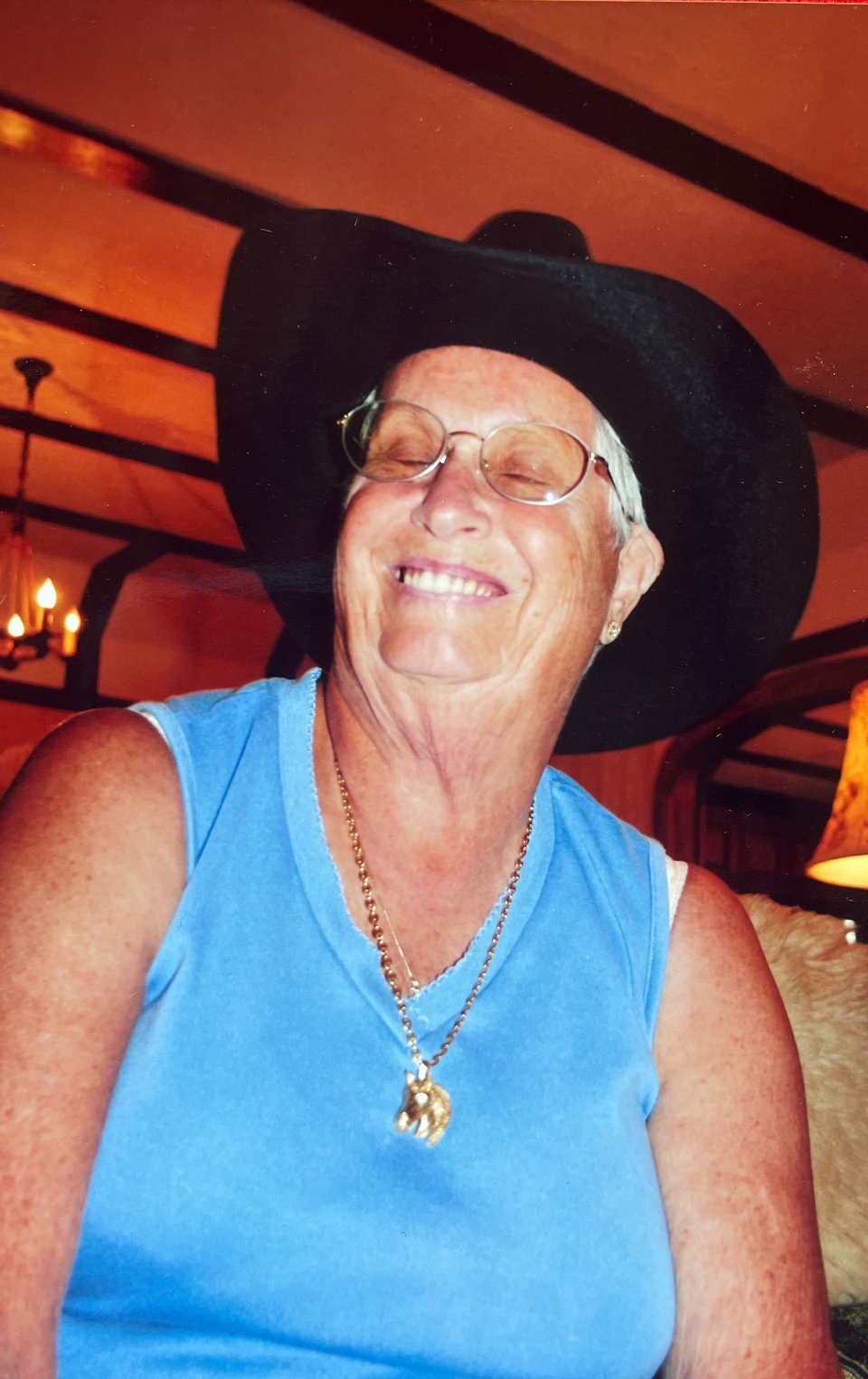 Image of Nana smiling in a blue shirt and a black cowboy hat, with a gold horse necklace hanging on her chest.