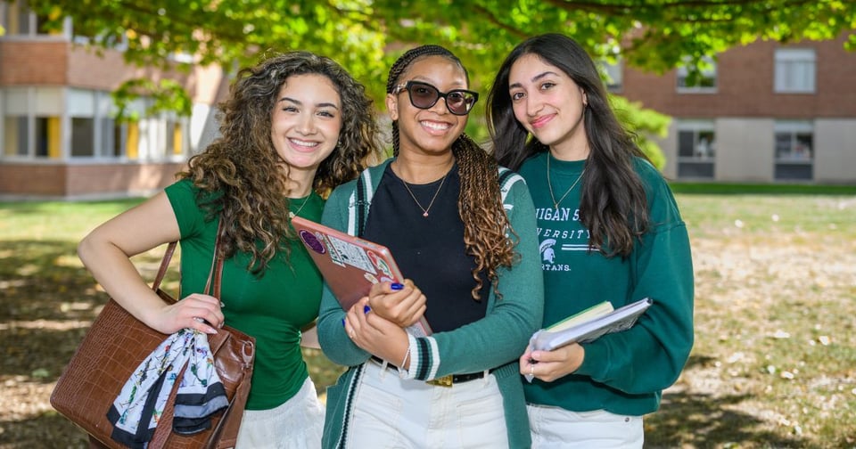 Three JMC students, wearing green sweaters, posing together outside of Case Hall.