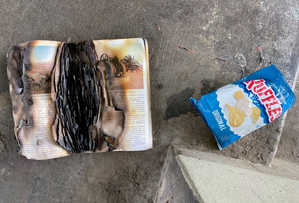 a burned book and bag of ruffles on the ground in a concrete stairwell