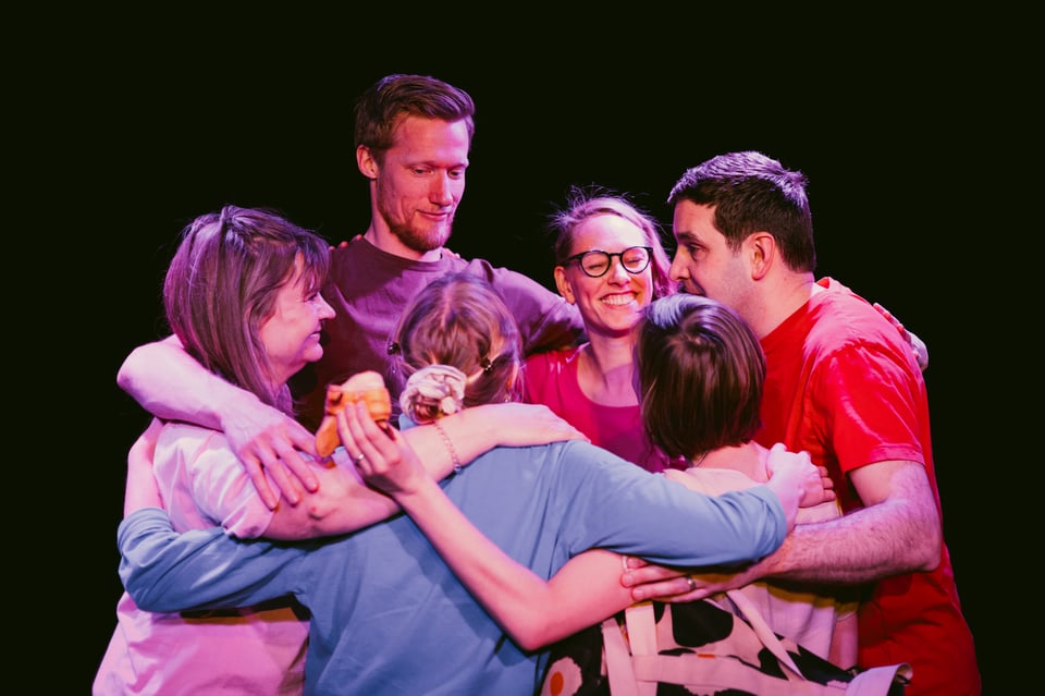 A photo from the warm up at a previous show with the ensemble (6 people) in a circle hugging each other.