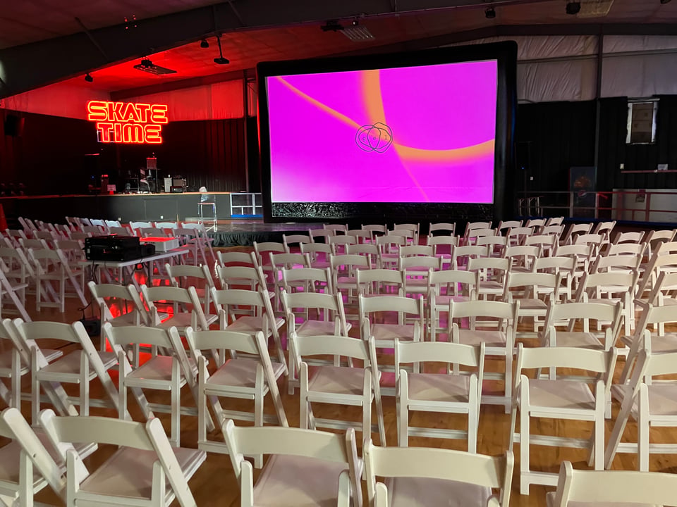 Gel 2026 setup: Rows of white folding chairs in front of a large projection screen showing the Gel logo superimposed over pink and orange gel images. A neone "Skate Time" sign is seen in the background.