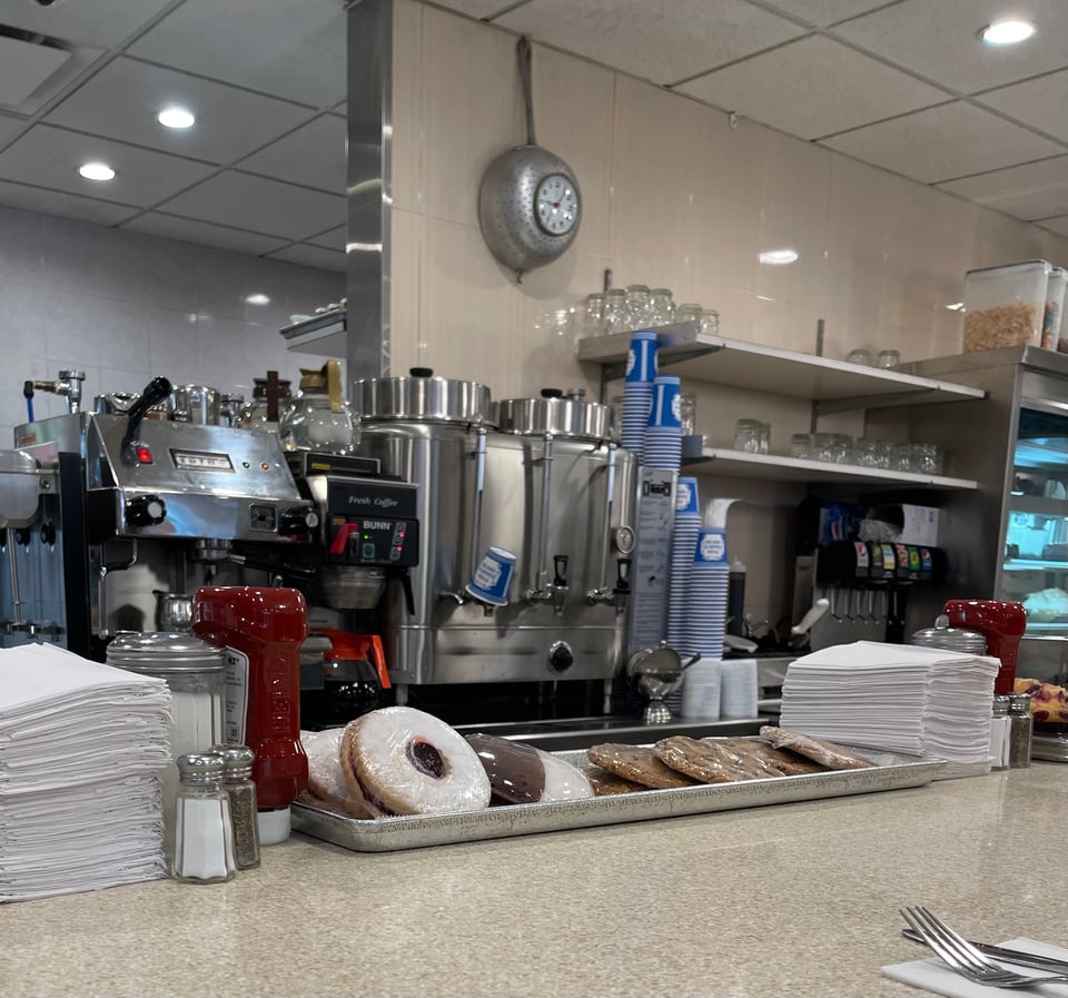 Interior of a coffee shop, with plastic wrapped cookies, coffee machine, and traditional blue and white NYC coffee cups