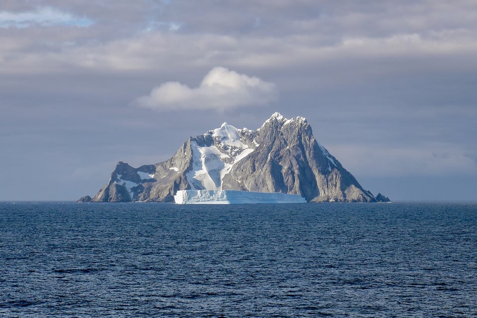 An isolated island in the Antarctic, snow on the peaks, surrounded by ice bergs, steep sided.