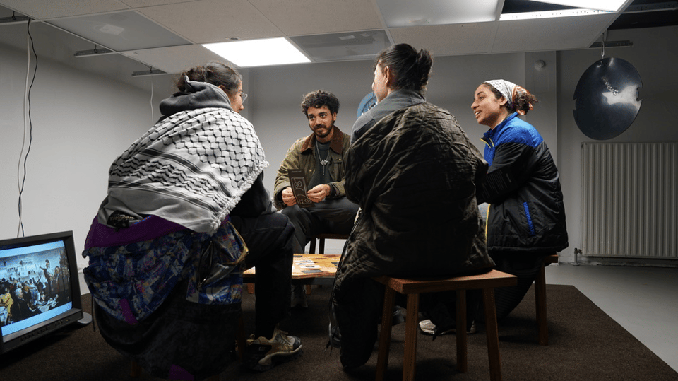 A group of people sit around a table filled with cards. They are playing the game "dissenting decisions"