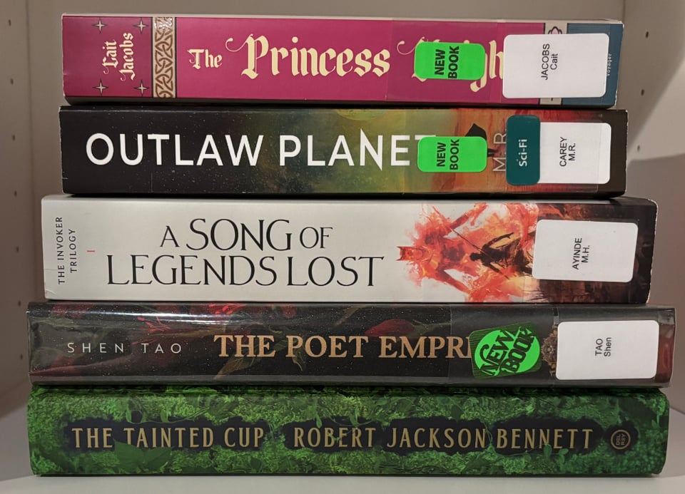 A stack of books, horizontal and spines out: The Princess Knight by Cait Jacobs, Outlaw Planet by M.R. Carey, A Song of Legends Lost by M.H. Ayinde, The Poet Empress by Shen Tao, and The Tainted Cup by Robert Jackson Bennett