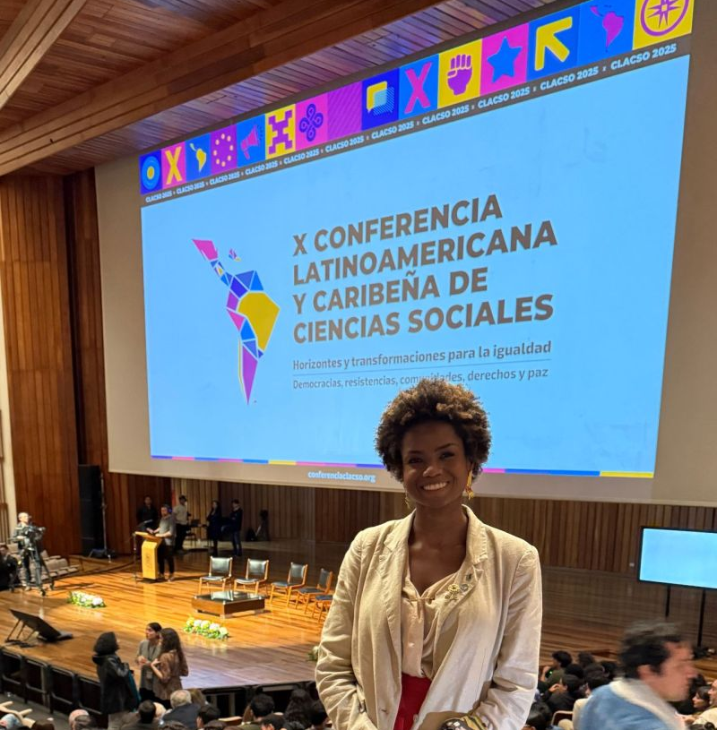 Nurianne posing with a big smile in front of a welcoming screen of the conference.