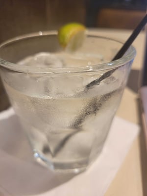 A mostly full gin and tonic on a cocktail napkin.