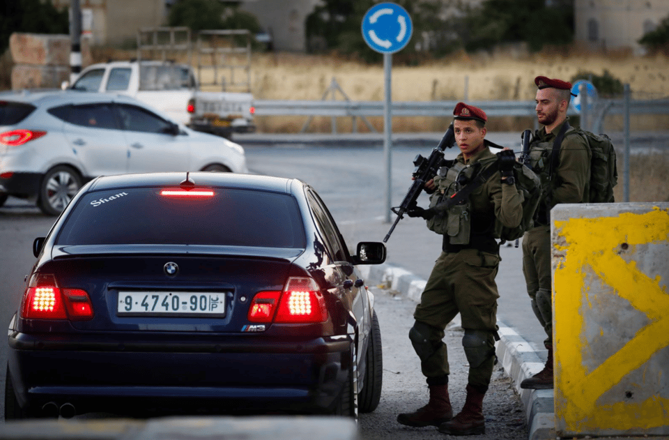 Two soldiers, one with a machine gun, next to a car
