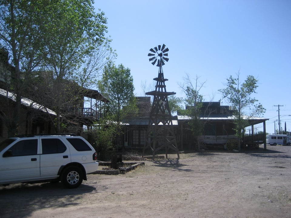 A parking lot surrounded by wooden buildings. A decrepit windmill looms over it.