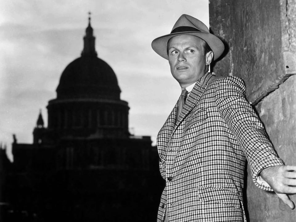 Richard Widmark in an old black and white movie, wearing a hat and suit, flattened against a wall looking desperate.