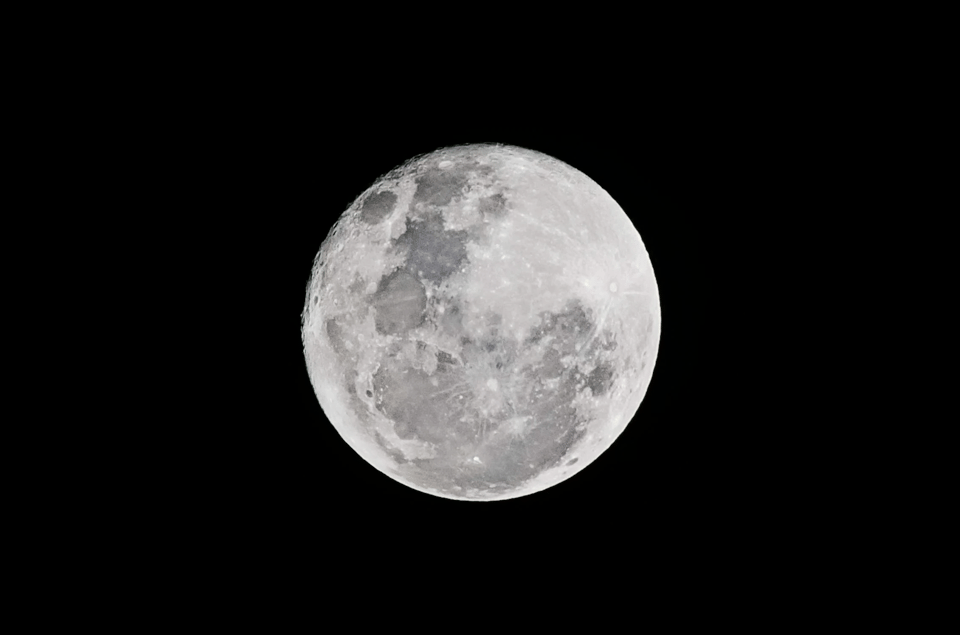 Photo of the moon on completely black and starless background. The moon is full and many small details are visible.