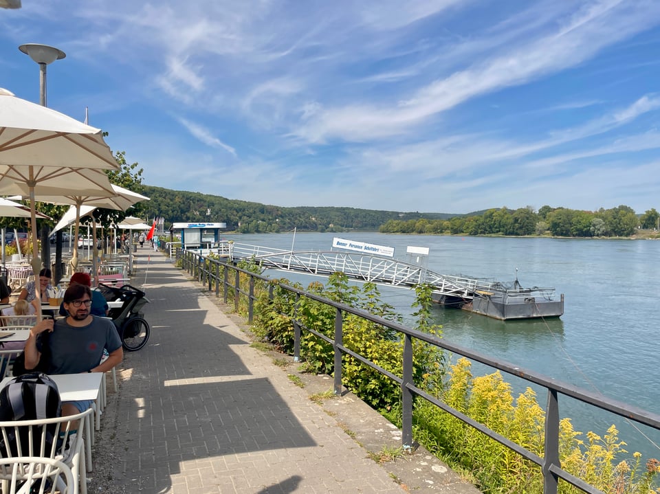 A man sits in a row of tables by the riverfront.