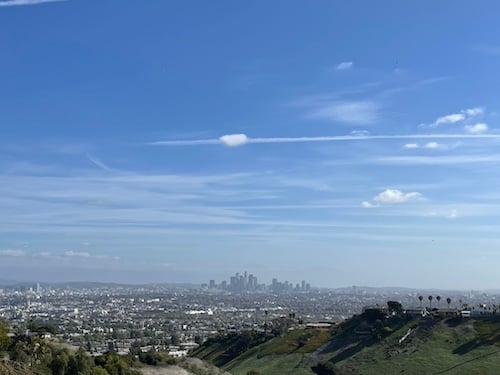 a view of downtown Los Angeles from across the city, blue skies and thin clouds with one small one in the middle of frame