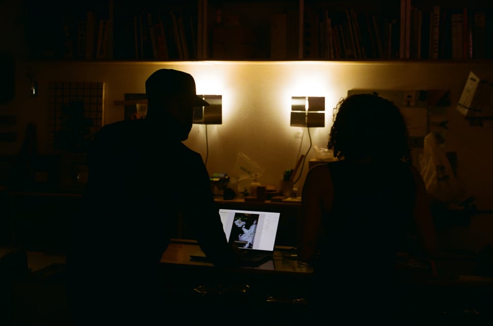 [Two people sit at a table with a laptop scanning books.]
