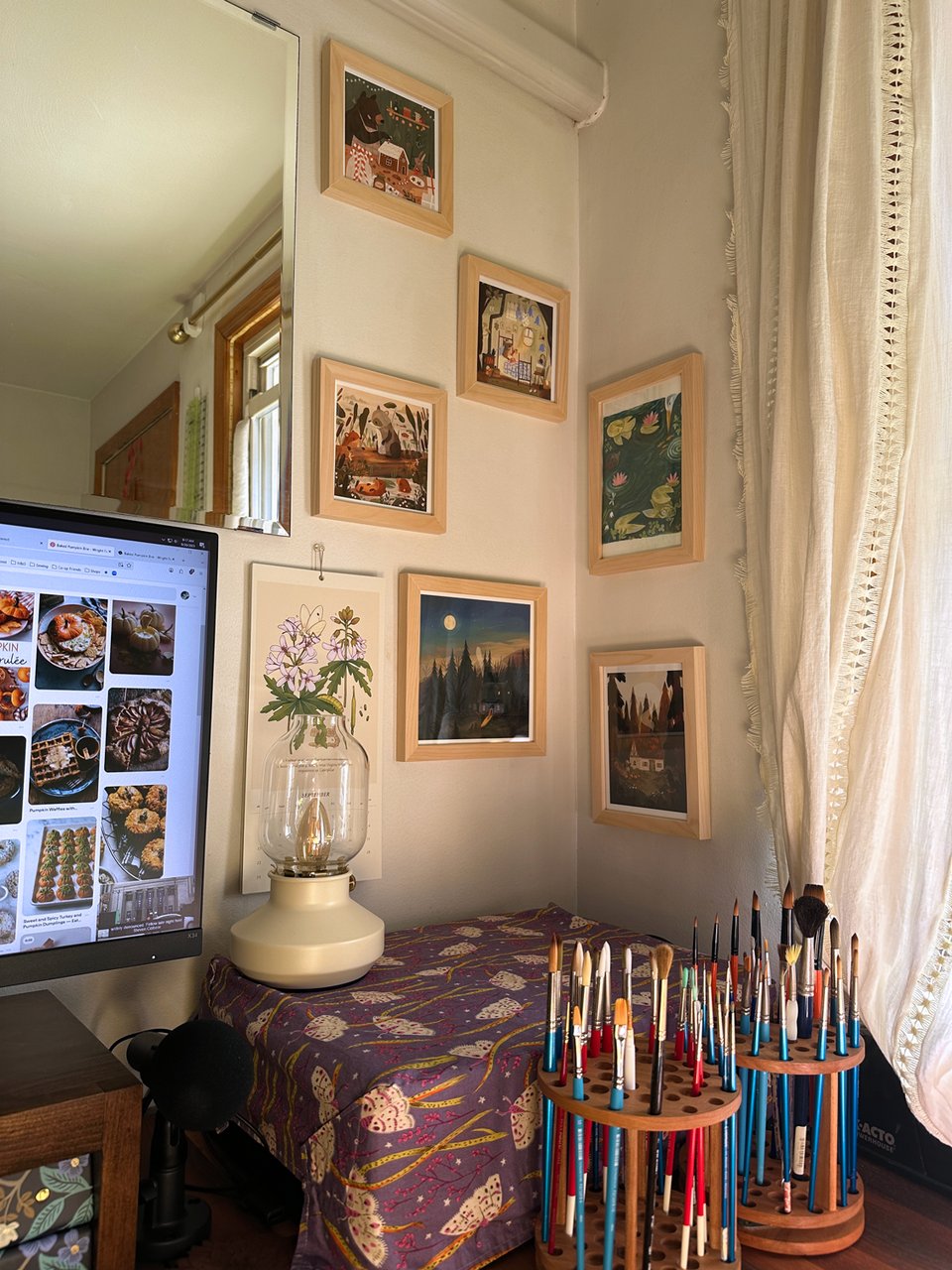 A corner of Jessi's studio. On the walls, there are several framed pieces of art by the artist Raahat Kaduji. They're all animal- and woodland-themed, made with mixed media. The effect is very cozy.