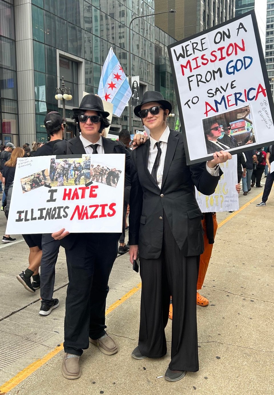 Two protesters dressed as the Blues Brothers, holding signs that read: I hate Illinois Nazis and We're on a mission from God to Save America.
