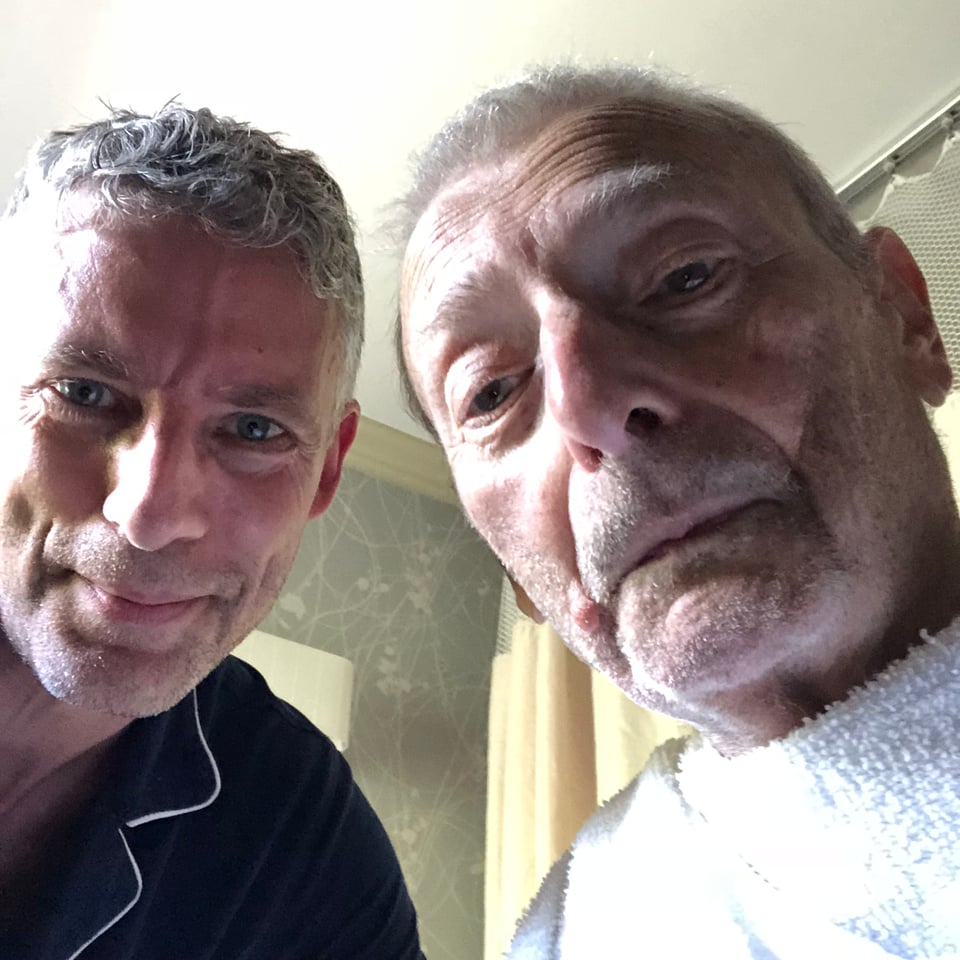 selfie of two white men, a 40-something man & his 80-year-old father; the older man has a white towel tucked into his collar