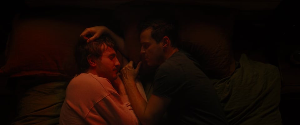 A screencap from the film All of Us Strangers, of the two male leads cuddling together in bed.