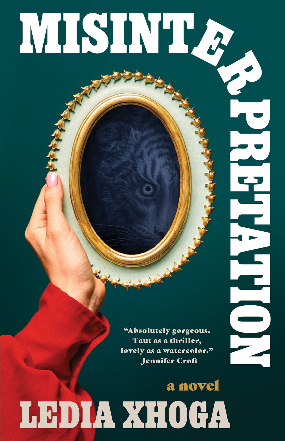 A white woman's hand, cuffed in a red blouse, holding up a white and gold enamel frame with a monochrome image of a tiger's face in shadow. Dark green background, white text