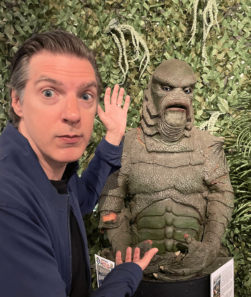 A human man points happily at a worn-down statue of the Gill-Man