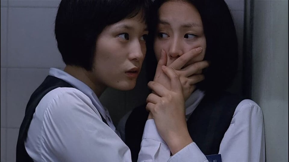 One Japanese schoolgirl holds her hand over another's mouth in Memento Mori.