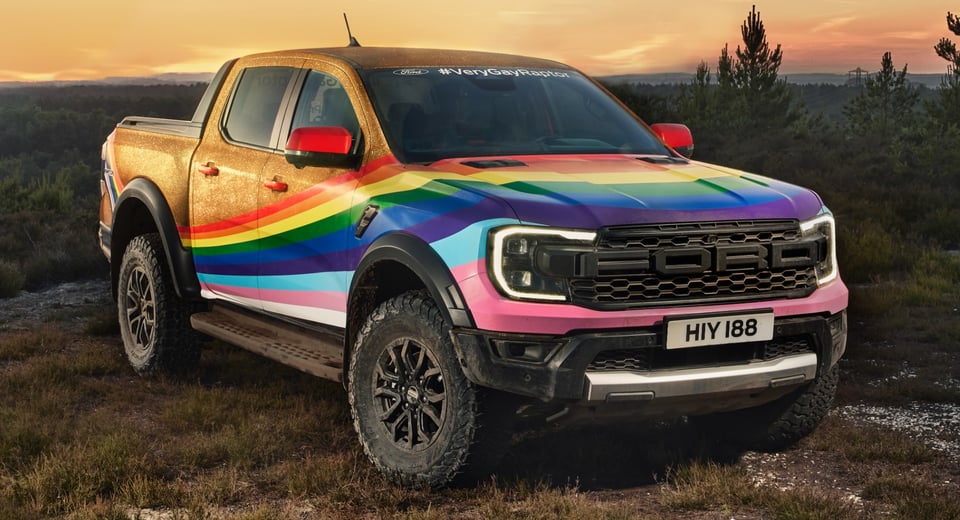A Ford Raptor pickup truck painted in a pride rainbow with gold bodywork. It has 'very gay raptor' on its windshield