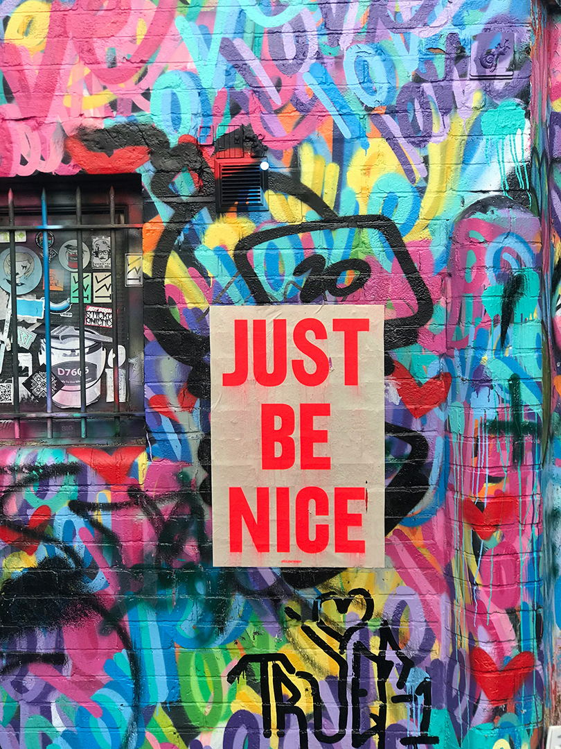 A multicolour graffitied wall bear the slogan "just be nice".