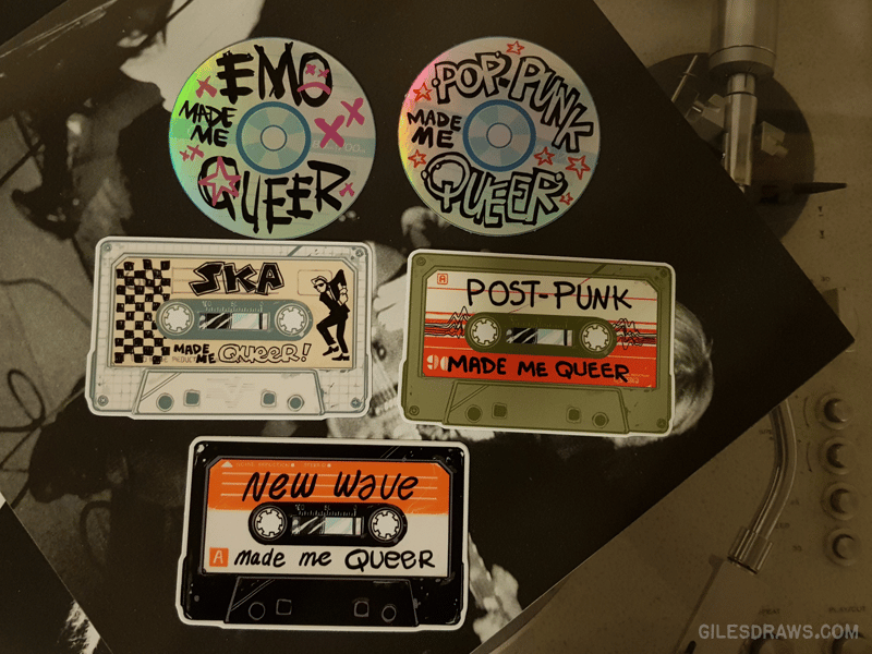 A photo of two CD stickers and three cassette tape stickers. The CDs say "emo made me queer" and "pop punk made me queer" and the tapes say "ska made me queer," "post-punk made me queer," and "new wave made me queer."