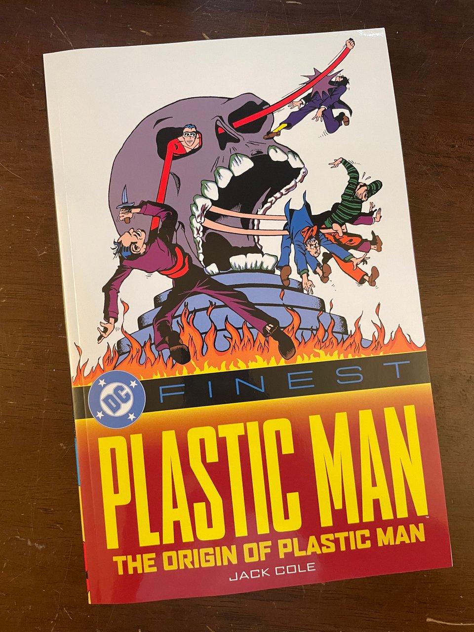 Photo of the cover to Plastic Man: The Origin of Plastic Man. Plas is beating up a bunch of thugs from inside a giant gray skull while a fire blazes at its base. Plastic Man is smiling, because he's a badass.