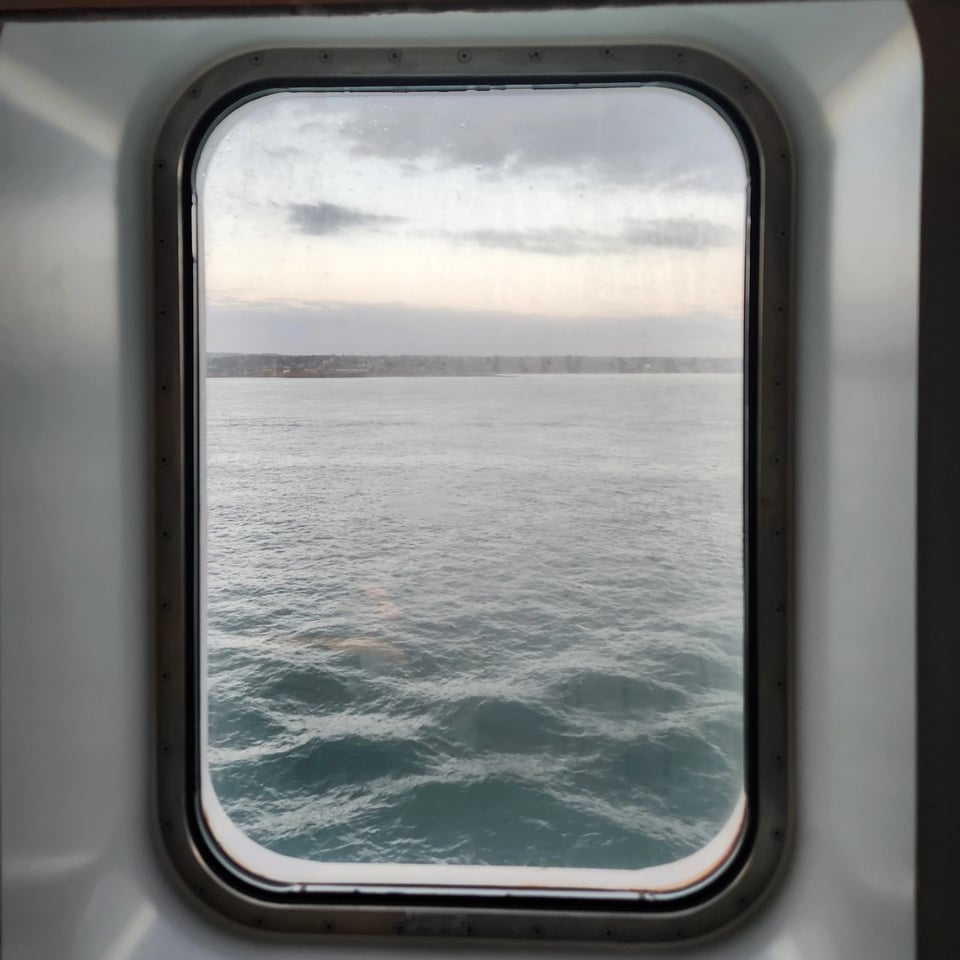 A rectangular porthole window showing the ocean and a spit of land.