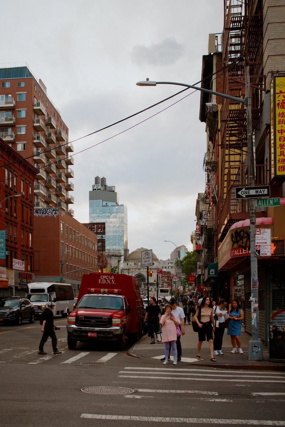 The streets of New York City at dusk, at Allen St. People walking all over, and busy.