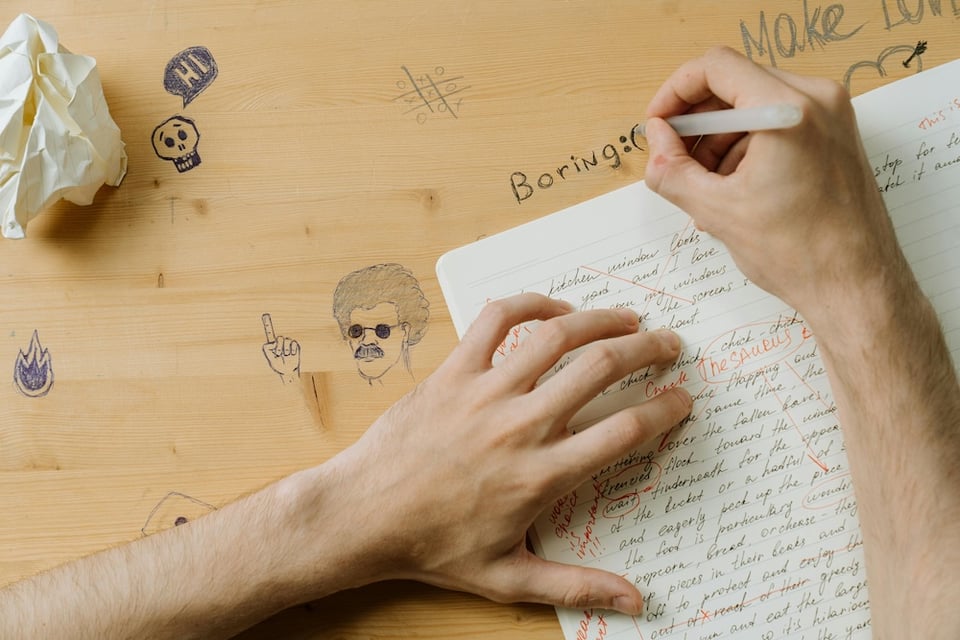 a person with a notebook open writing "boring" on a school desk