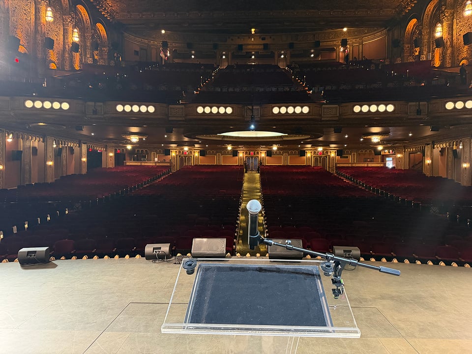 View from the stage behind the lectern and mic looking out at an empty, beautiful, baroque hall before students and families are let in.