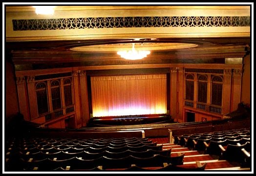 An image of an old cinema, with a curtained off screen overlooked from balcony seating.