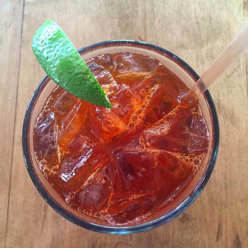 An overhead view of a glass of Thai Iced Tea and a lime wedge on the top left edge of the glass. The colors are orangey-red for the tea and a green for the lime wedge. This photo was taken at Chiang Mai, a now-shuttered Thai restaurant in Portland, Oregon.