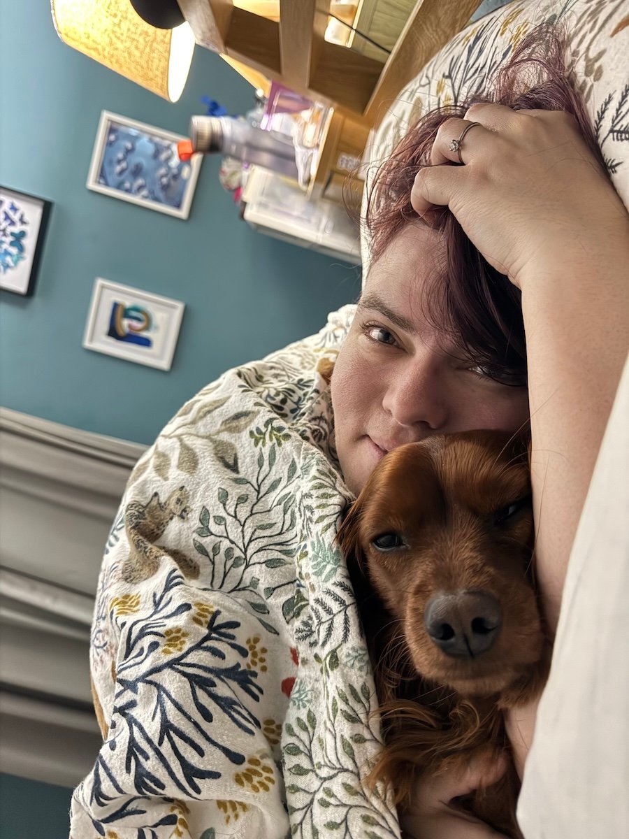 A beautiful lady holds a beautiful dog whilst lying in bed.