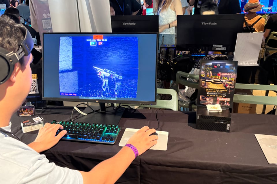 A person with curly hair is playing games at a booth. It appears to be a first person shooter with no enemies and looks strangely haunted. The game is No Players Online.