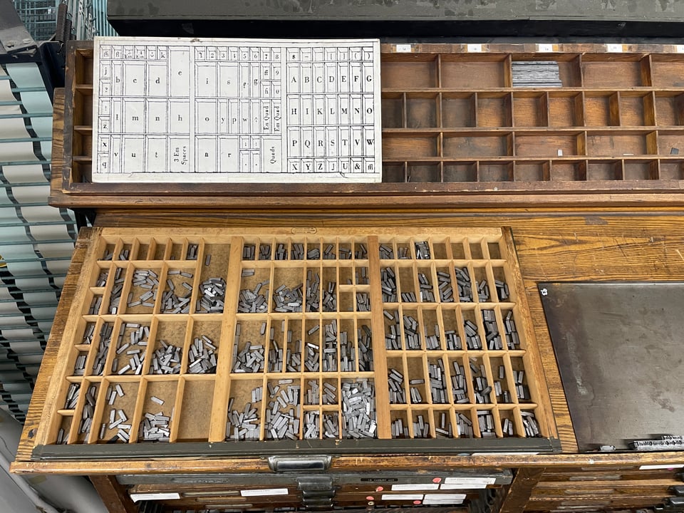 A letterpress workstation shows a wooden case full of metal characters of type.